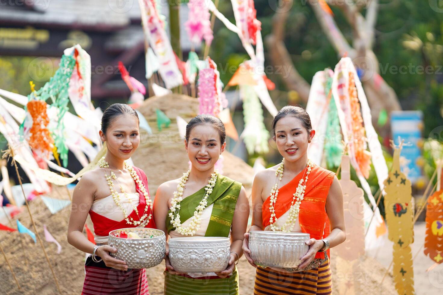 Portrait of Beautiful rural Thai woman wear Thai traditional dress acting and hold a silver vintage bowl for photo shoot on pile of sand in temple at the Songkran festival.