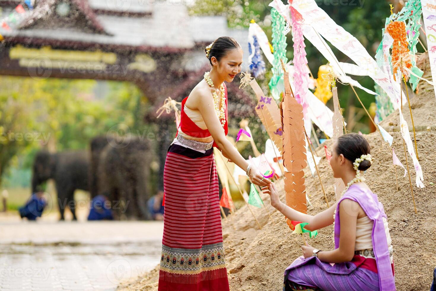 Beautiful Thai young lady ware Thai traditional dress give a small paper flags to her friends to help place in the sand in temple at the Songkran festival. photo