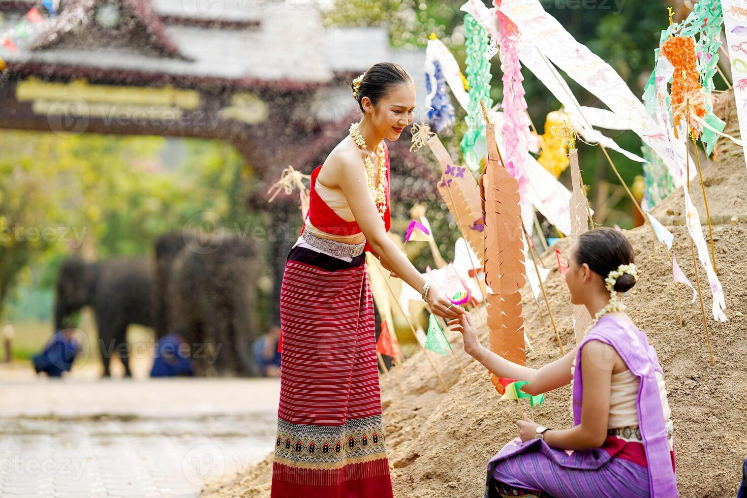 hermosa tailandés joven dama mercancía tailandés tradicional vestir dar un pequeño papel banderas a su amigos a ayuda sitio en el arena en templo a el Songkran festival. foto