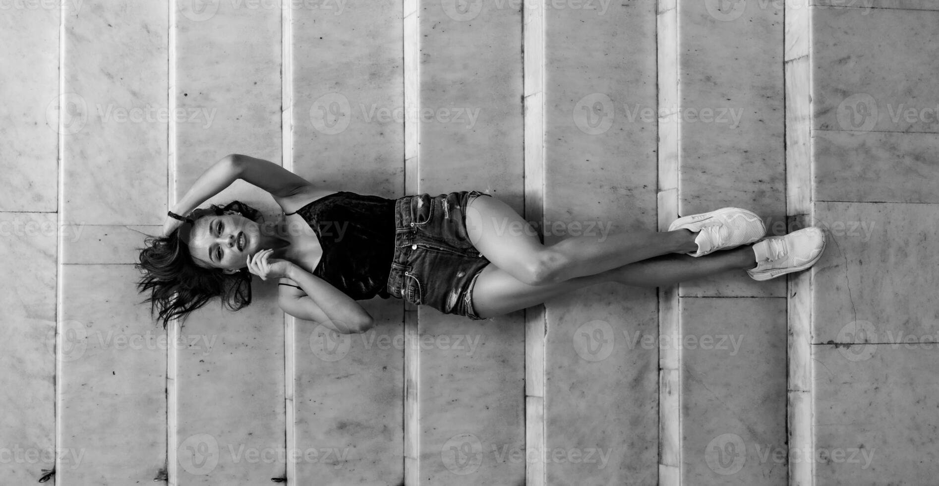 Portrait of a beautiful woman in black top and jeans shorts. Urban style modern photo. Black and white portrait. View from above. Horizontal portrait. photo