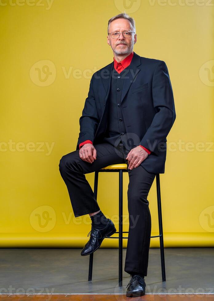 Content senior business man smiling in a dark suit. Handson legs . Red shirt. Confident. Business style concept photo