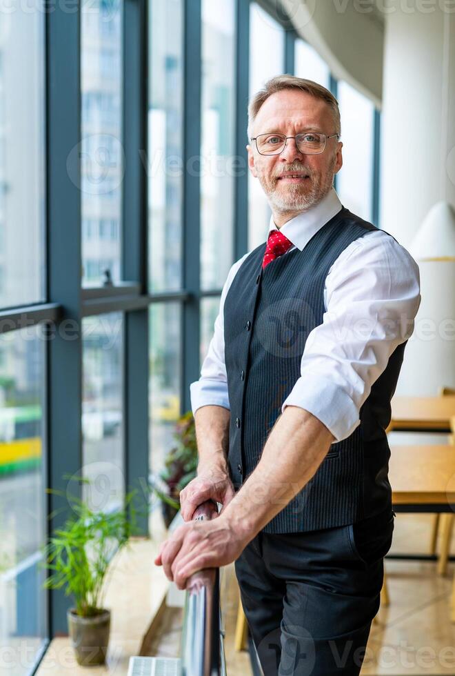 Businessman wears neatly white shirt and posing near big window with city view looking away. photo
