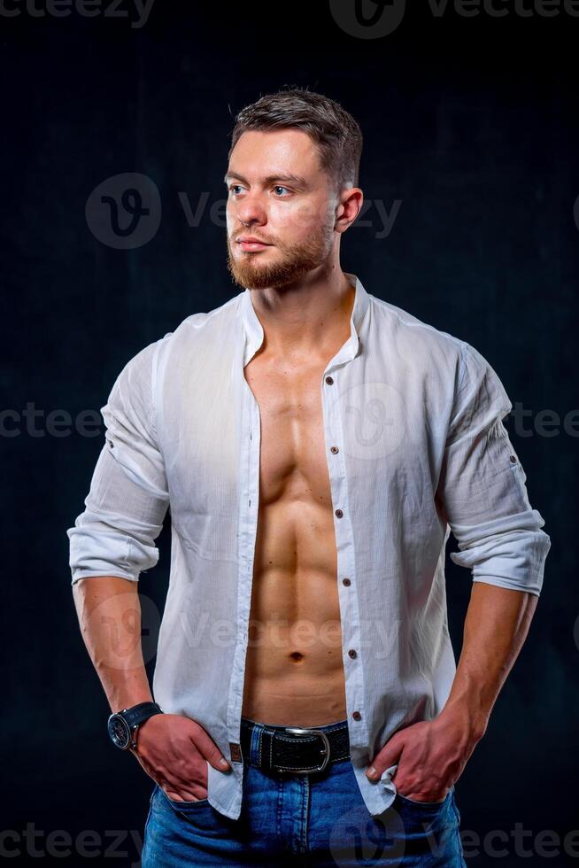 atlético hombre en blanco desabrochado camisa posando en contra oscuro antecedentes. foto