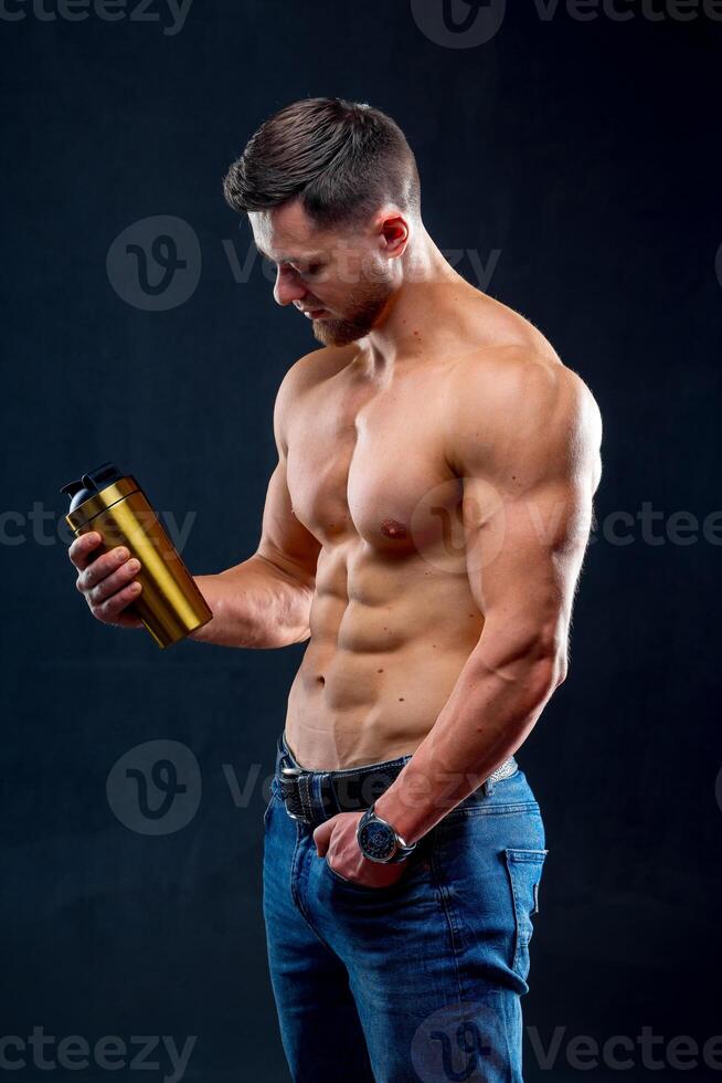 Portrait of a handsome halfnacked bodybuilder man with a sport bottle of water. Man posing on dark background. photo