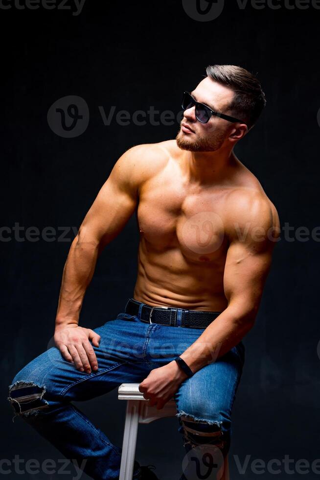 Athletic body. Half turned model guy is posing to the camera in the dark grey background. Full size photo. Strong muscular man. Closeup. photo