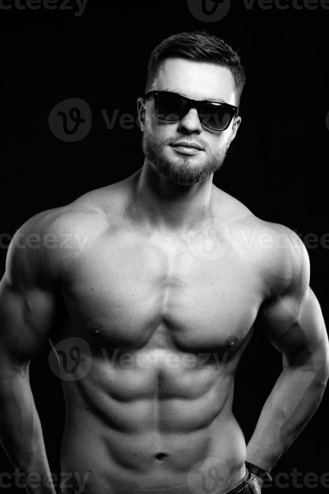 Muscular guy with naked torso posing with hands on waist. Studio photo. Portrait of a handsome man in jeans. Black and white. photo