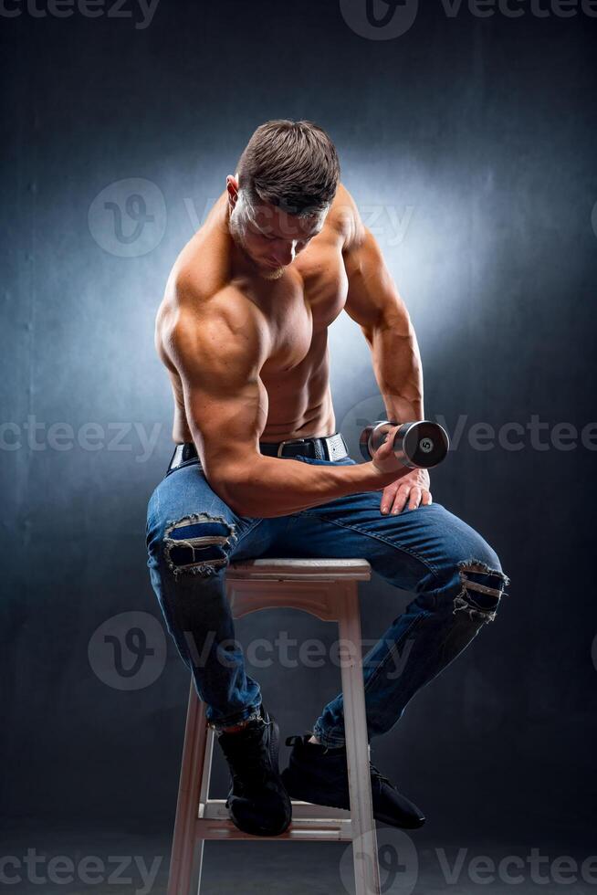Man with perfect body pumping up muscles with barbell in hand. Athlete sitting on high chair. photo