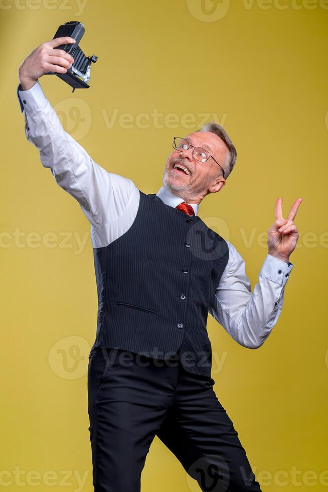 Senior man looking at camera while taking silly face selfie waving to the camera photo