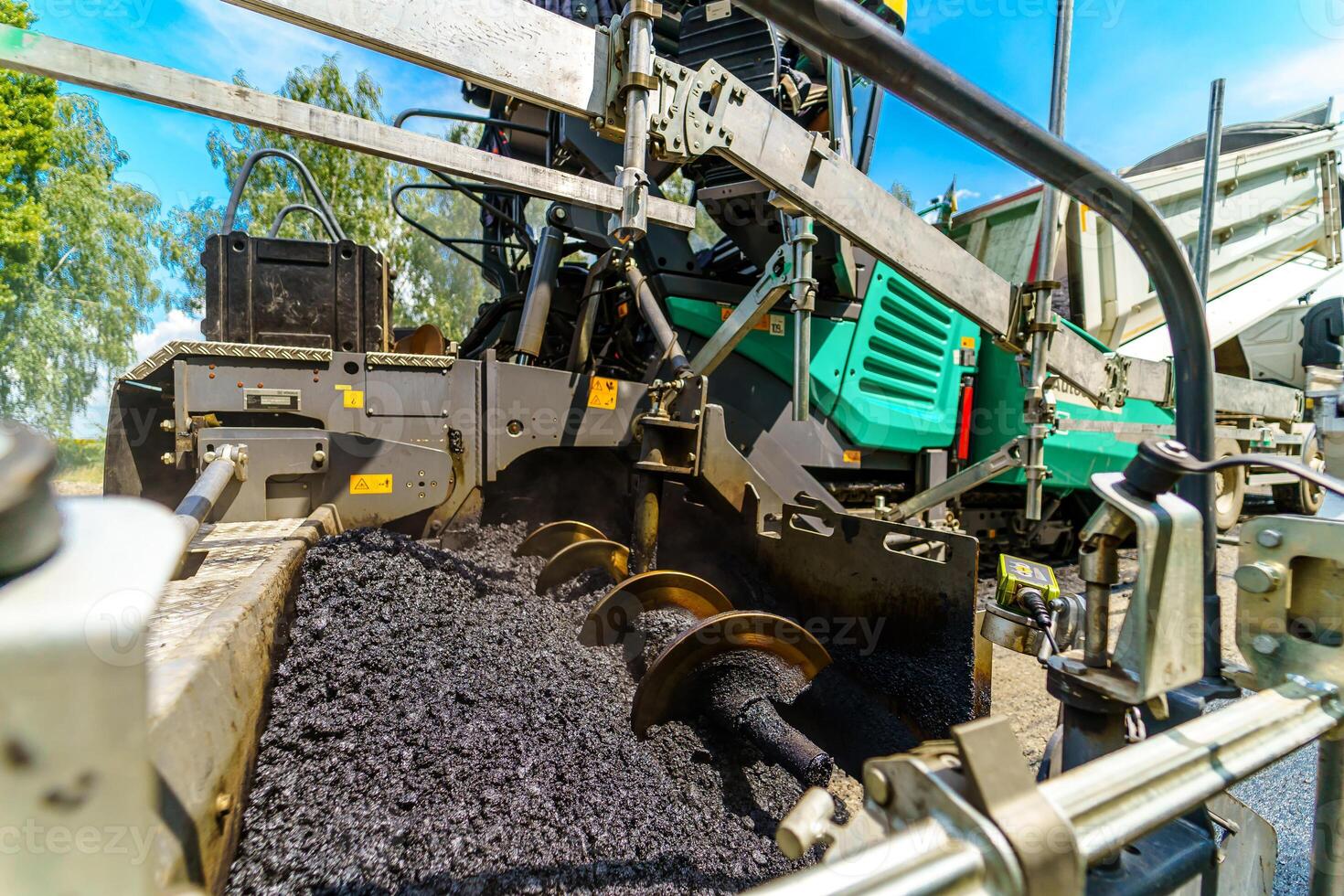 Cropped photo of machine with fresh asphalt. Flattering asphalt. Selective focus on heavy technic.