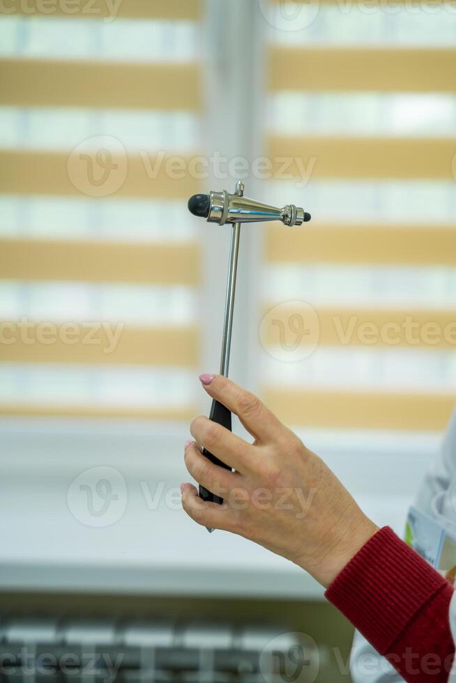 Doctors hand holding reflex hammer toward camera, focus on the foreground, on the hammer. photo