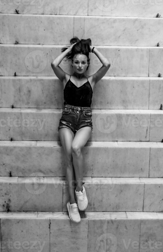 Fashion and style. Beautiful brunette lying on the steps. View from above. Black and white portrait. Vertical photo. photo