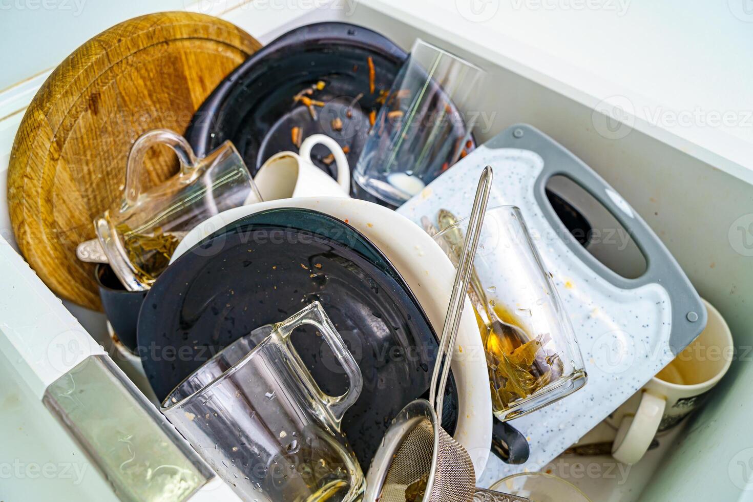 Pile of dirty dishes like plates, pot and cutlery in the white granite sink. photo