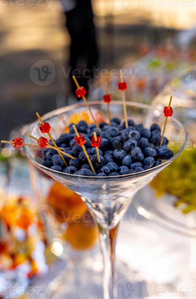 Blueberries in glass. Wooden piks in berries. Catering on wedding. Wedding banquet table. Sweet table with fruit, wedding catering. Fruit bar on party. photo