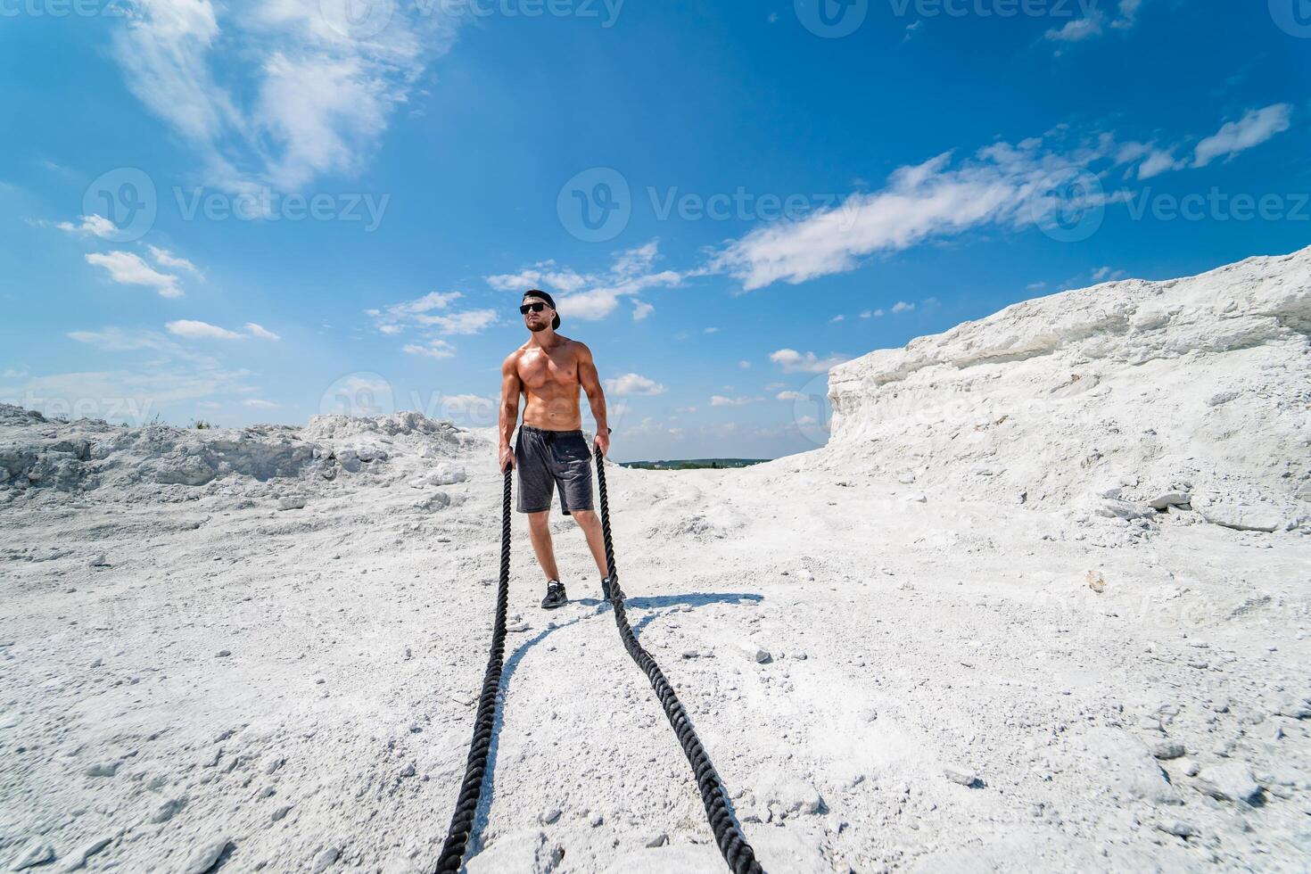 Handsome strongman walks up a quarry. White landscape. . Photoshoot in a quarry. Outdoor sports concept. Workout with ropes. photo