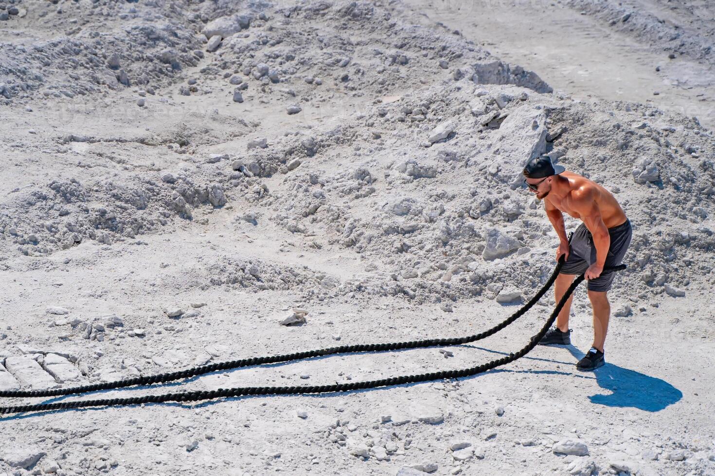 Heavy training in a quarry. Intense workout with ropes in white mountains. Strong attractive bodybuilder. Lifestyle. White landscape. photo