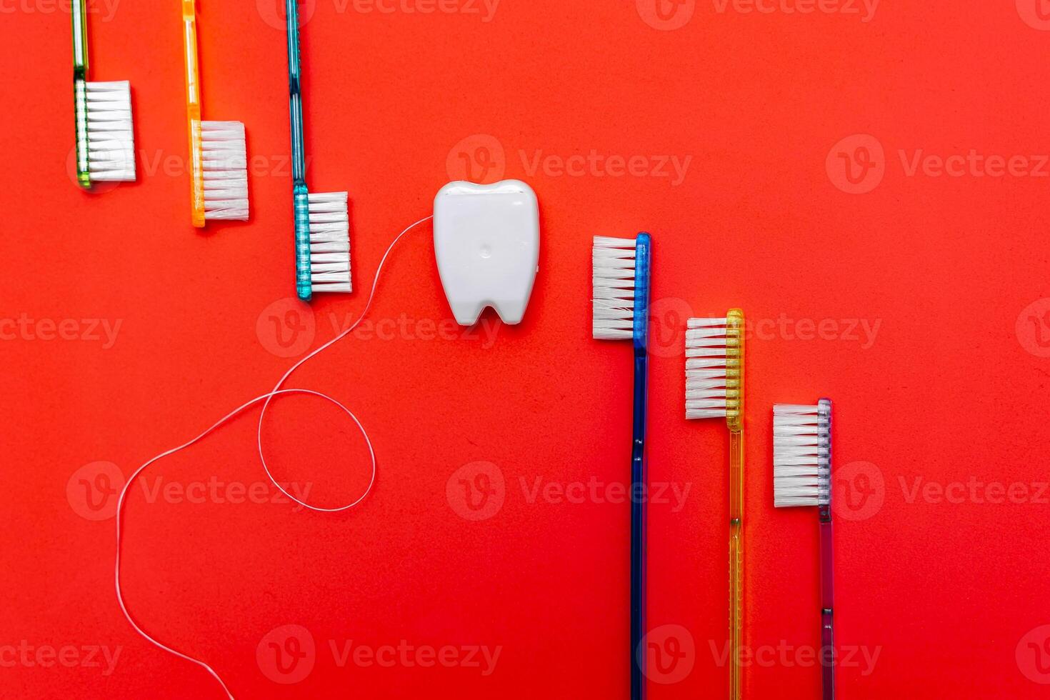Six tooth brushes in raw near toy tooth. Red background. Dental concept. photo