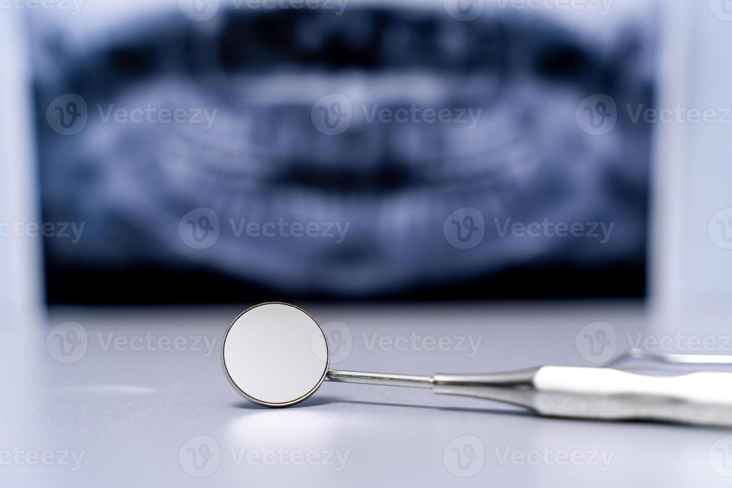 Dental mirror on front view. Jaw x-ray over blurred background. Healthy teeth concept. photo