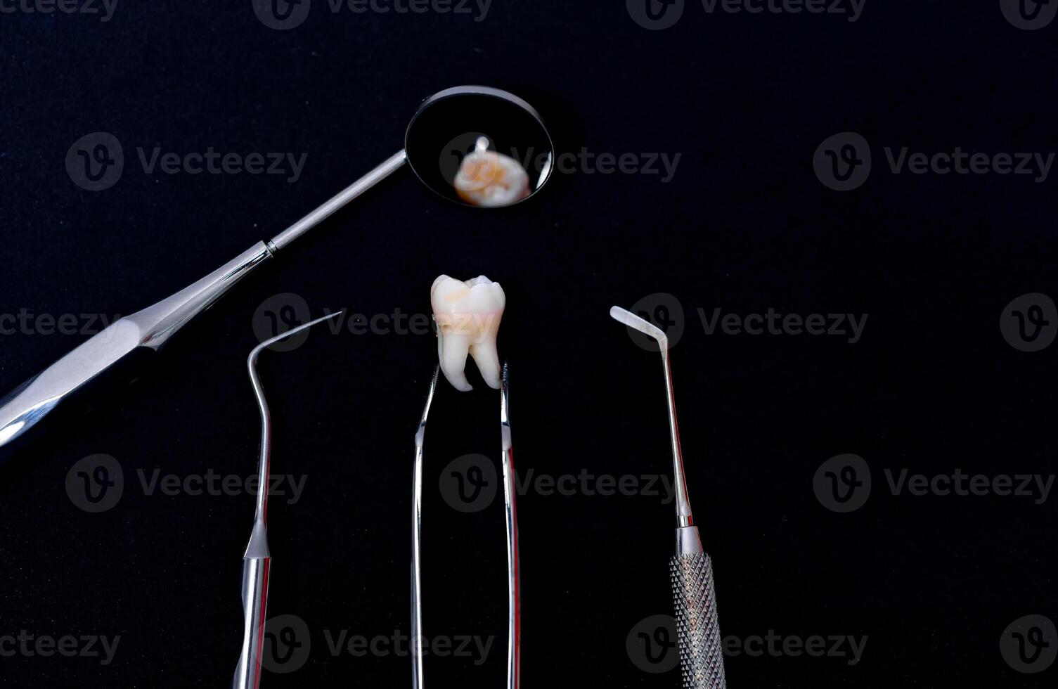 Dental instruments around ceramic tooth model. Black background. Art photo. photo