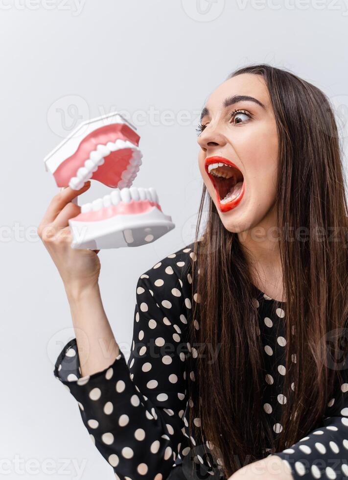 Funny girl toing with dental jaw on white background. Opened plastic jaw. Roaring girl with funny emotions. photo