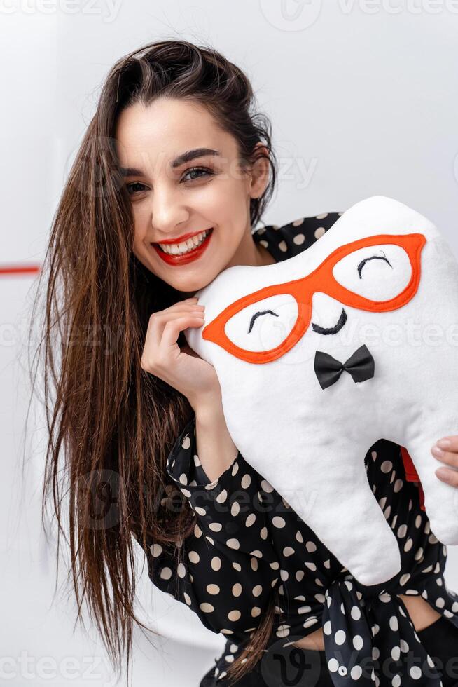 Portrait of a smiling girl with soft toy in hands. Tooth shaped soft toy. photo