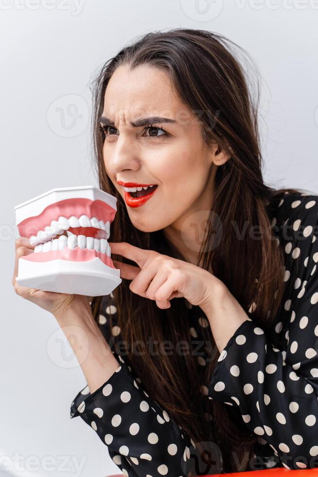 Woman with surprised face and opened mouth. Young girl holding opened educational dentist jaw near face. Dental concept. Funny emotions. photo