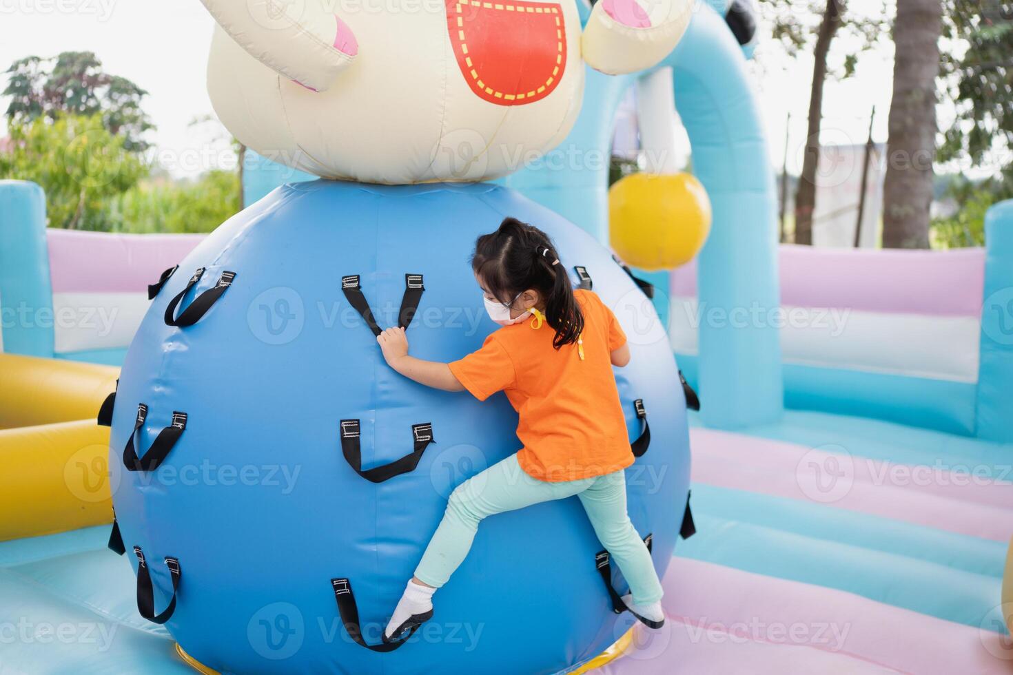 A little girl is climbing a blue inflatable obstacle. The obstacle is blue and has a yellow and pink section photo