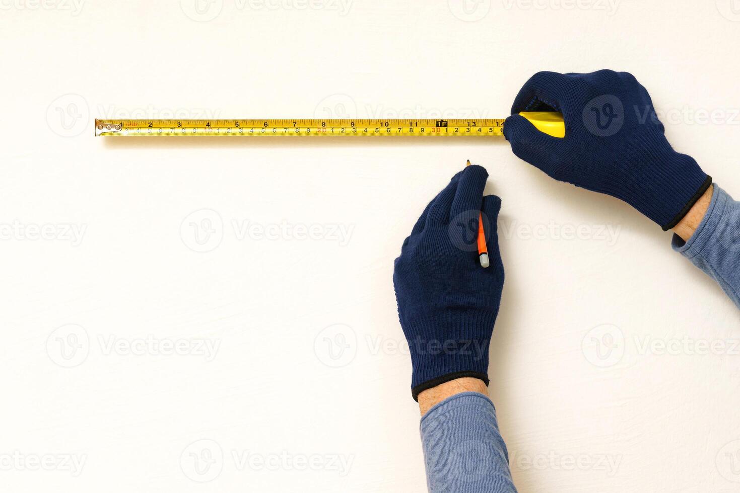 Builder's hands with measuring tape and pencil on white wall. photo