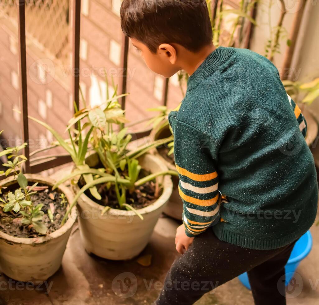 linda 5 5 año antiguo asiático pequeño chico es riego el planta en el ollas situado a casa balcón, amor de dulce pequeño chico para el madre naturaleza durante riego dentro plantas, niño plantando foto