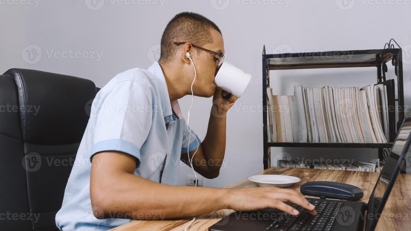 a man drinking from a cup. person having a coffee in front of him while he works. photo