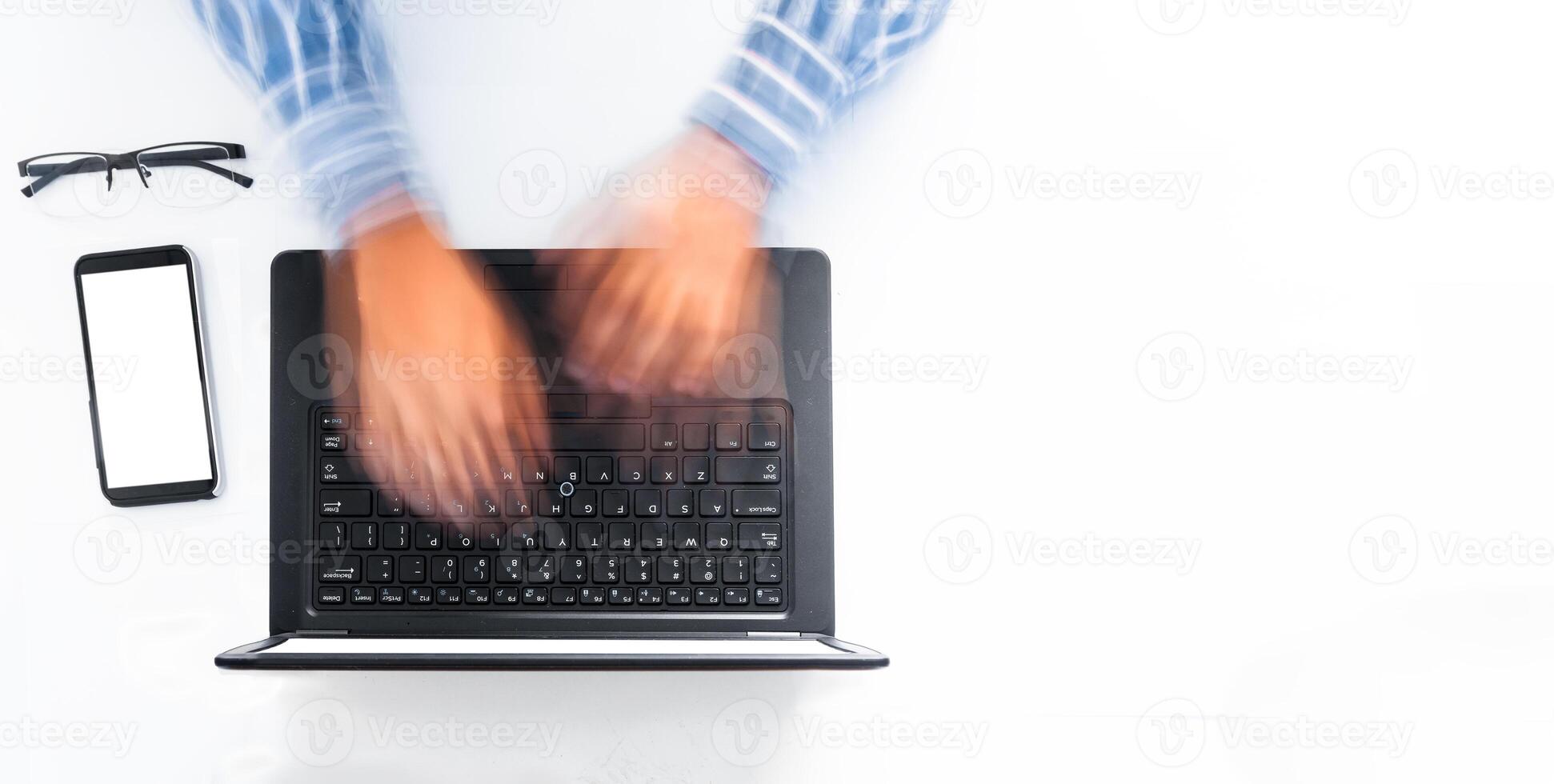 overhead shot of a man's hands typing fast on a laptop on a white desk. programming concept. office work. photo