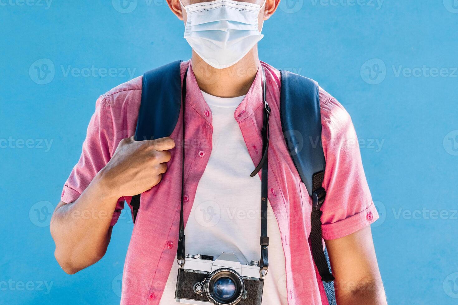 man traveler with vintage camera and holding a backpack wearing a protective mask. photo