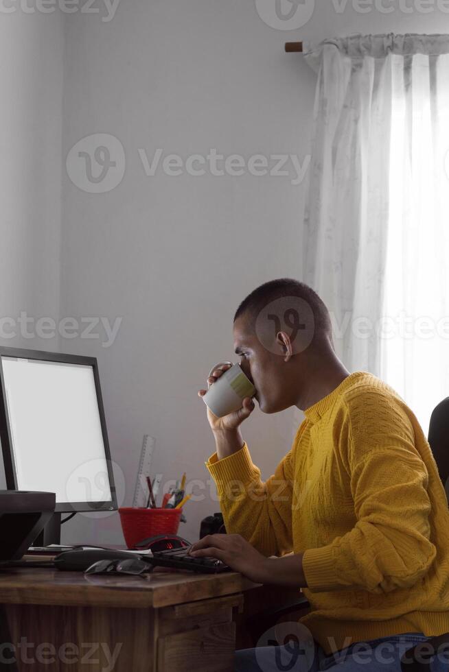 Hispanic man drinking from a cup working on a computer photo