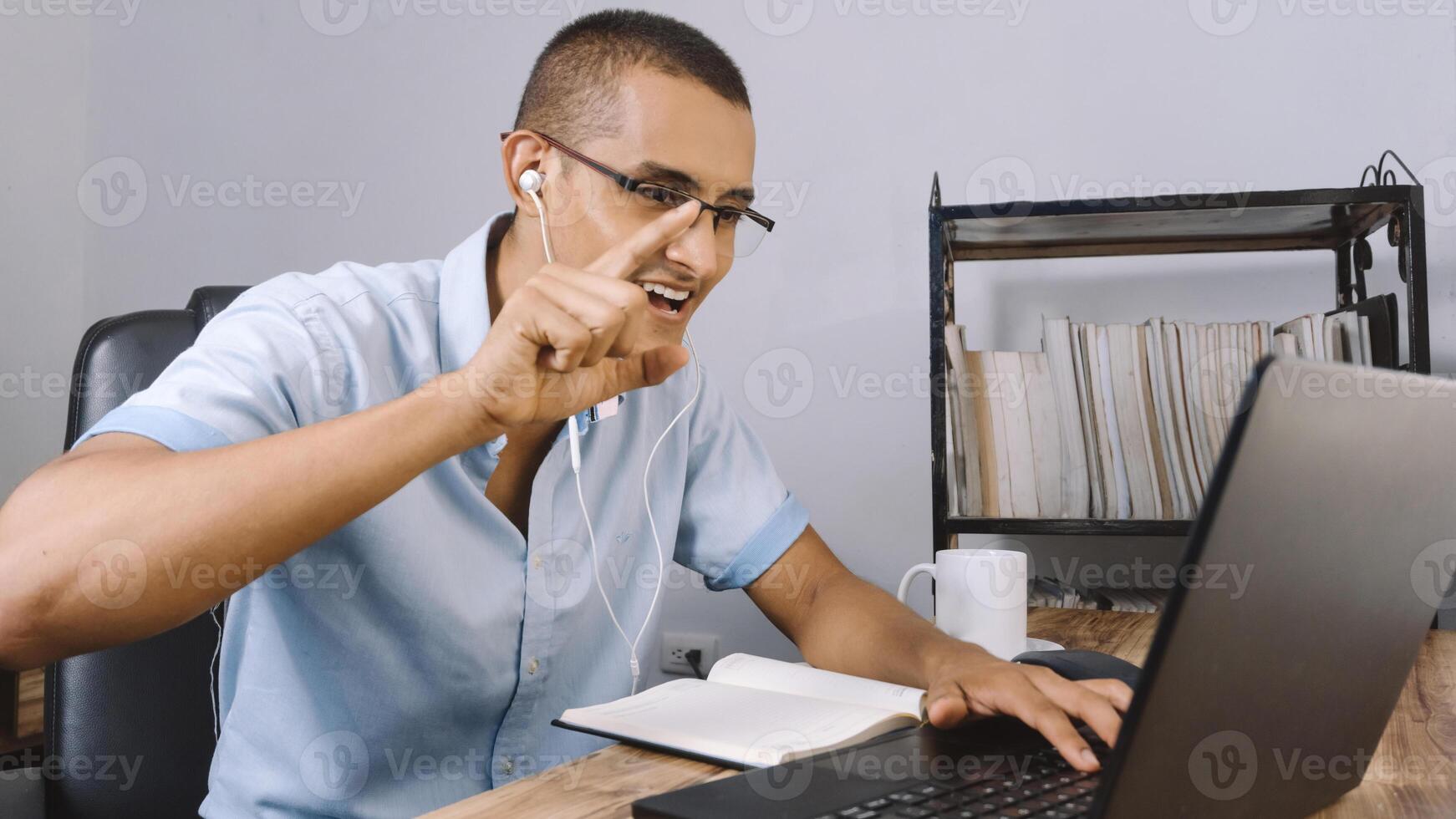 young latinx man raises his hand and finger to give his opinion in a virtual class. Hispanic using a laptop concept webinar and technology. photo