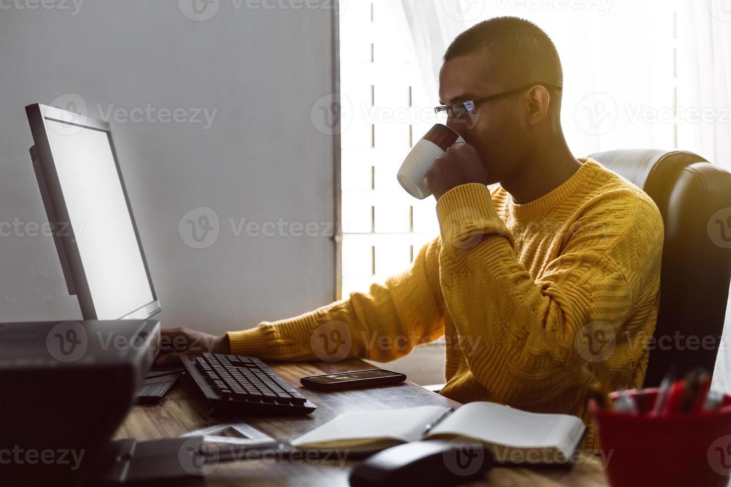 latin american young adult man have a cup of coffee while working on his desktop computer. photo
