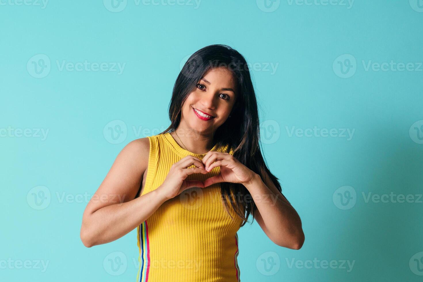 joven Hispano mujer con Derecho pelo y sonriente en amor haciendo corazón símbolo forma con manos. foto