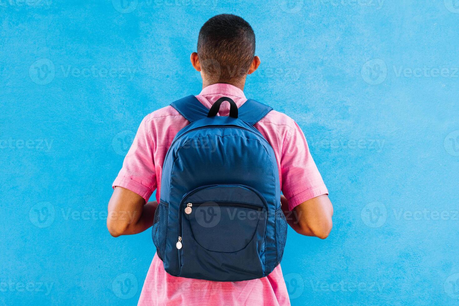 man from behind with a backpack in front of a blue wall. photo