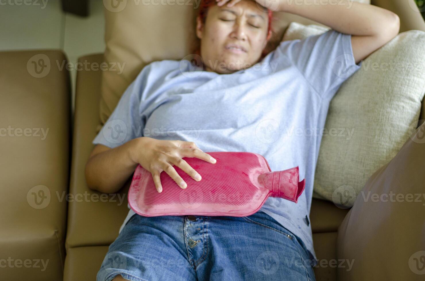 Top view. Young Asian woman lies on the sofa using a hot water bag to relieve menstrual cramps. photo