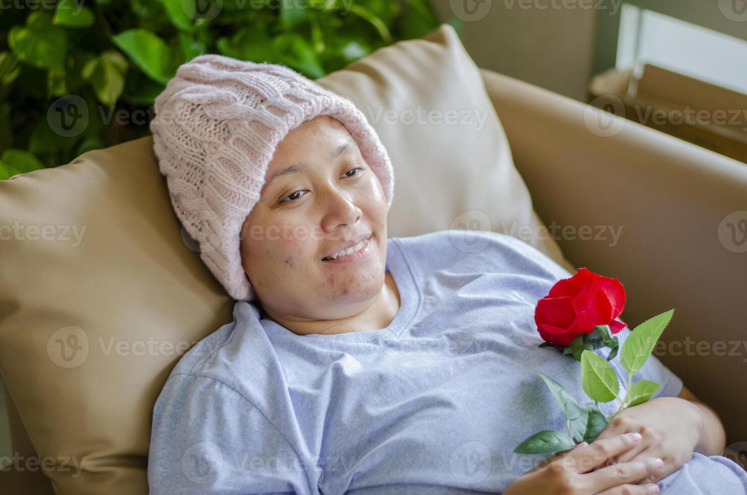 Asian woman with cancer, she is lying on the sofa in the living room, smiling and happy after receiving roses as encouragement. photo