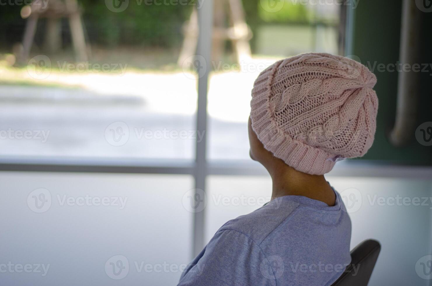 Asian woman with cancer, sitting with her back turned and looking out the window photo