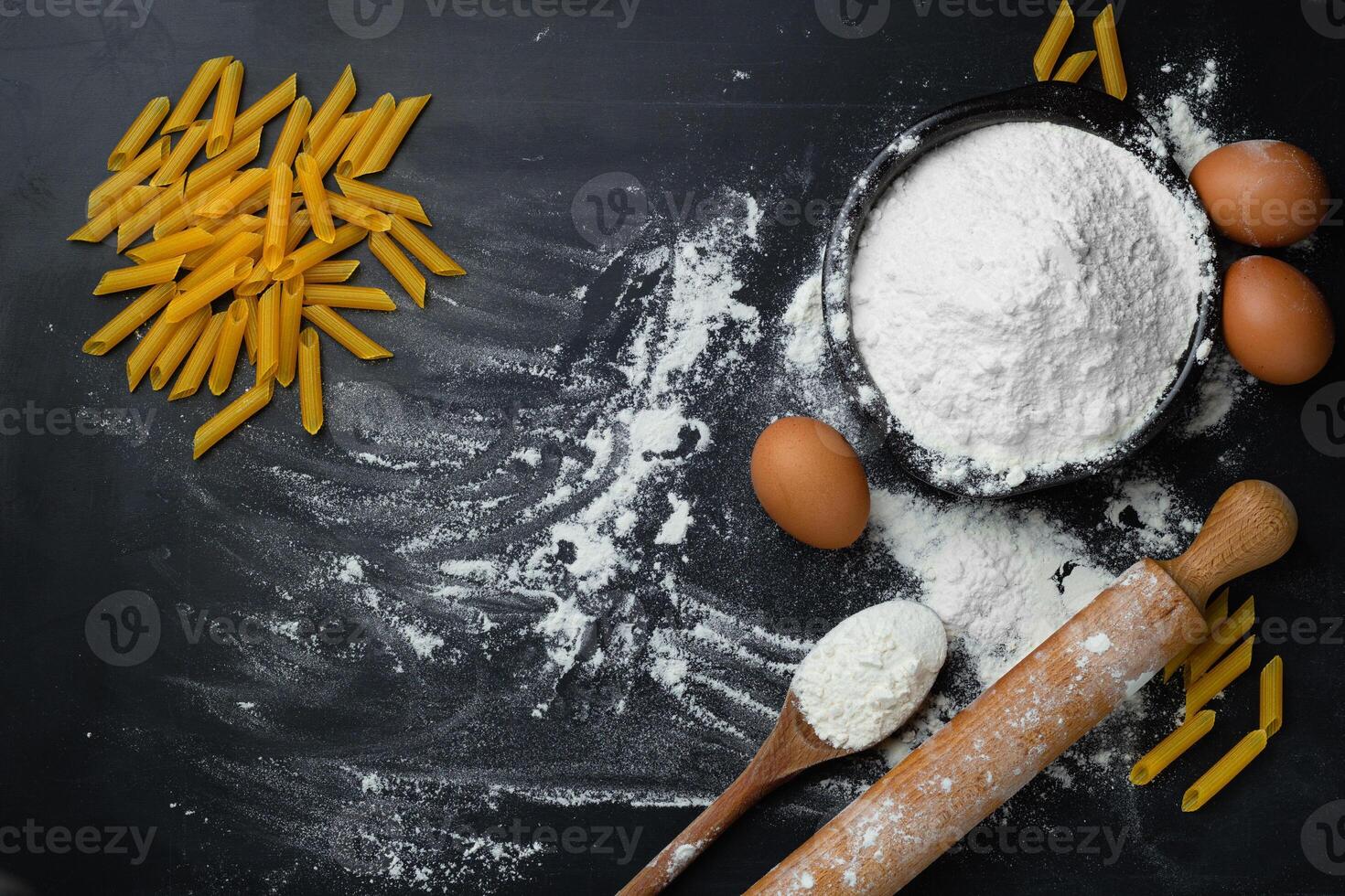 Raw homemade pasta penne on dark background with eggs and flour. Top view. photo
