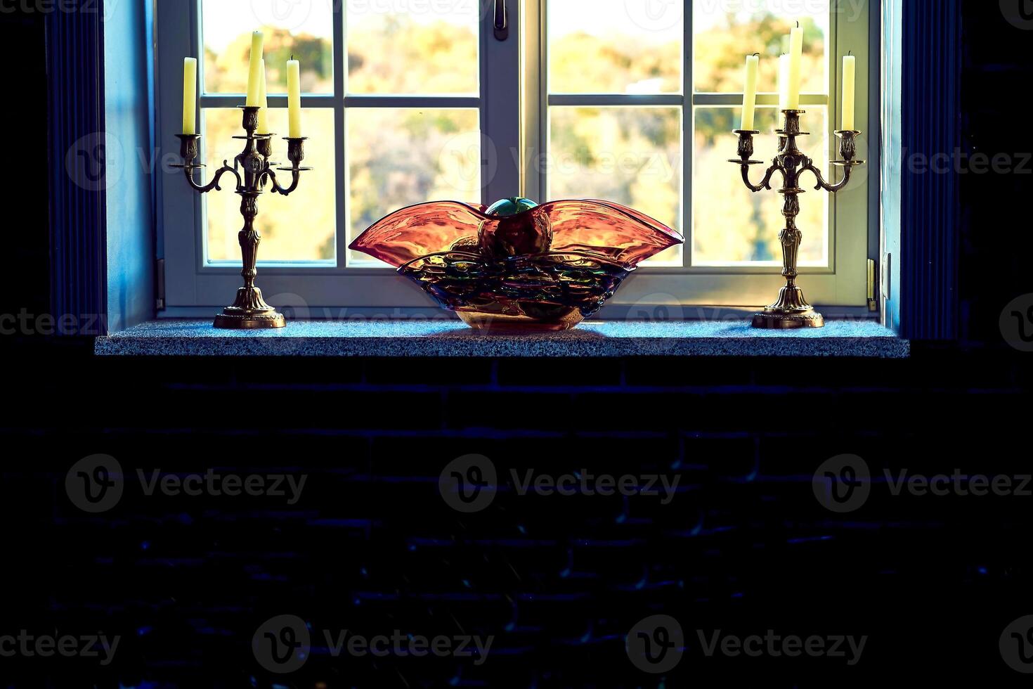 Window to the garden with candlesticks and an orange vase on a dark photo