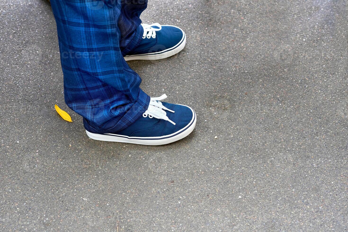 Legs of a schoolboy in blue plaid trousers and sneakers with laces photo