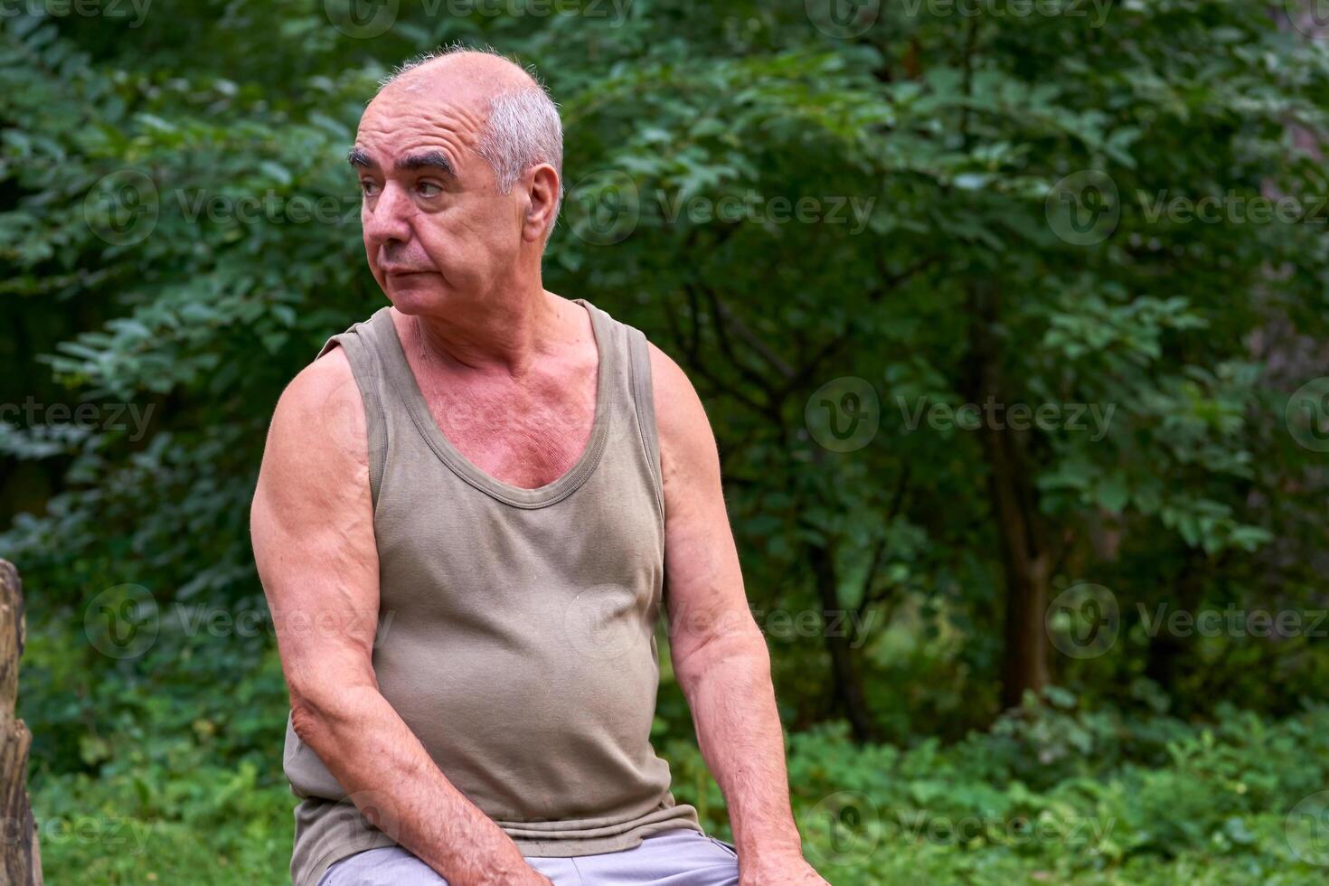 Pensive elderly man pensioner in a T shirt in a forest on a picnic photo