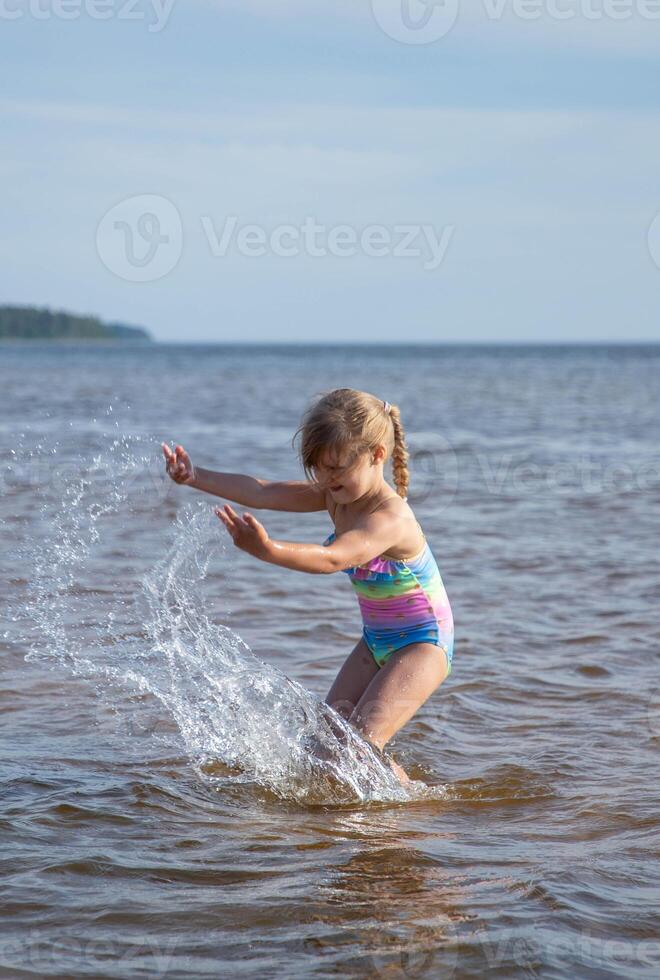 joven contento niño niña de europeo apariencia años de 6 6 teniendo divertido en agua en el playa y salpicaduras, tropicales verano vocaciones,vacaciones.a niño disfruta el mar.vertical foto. foto