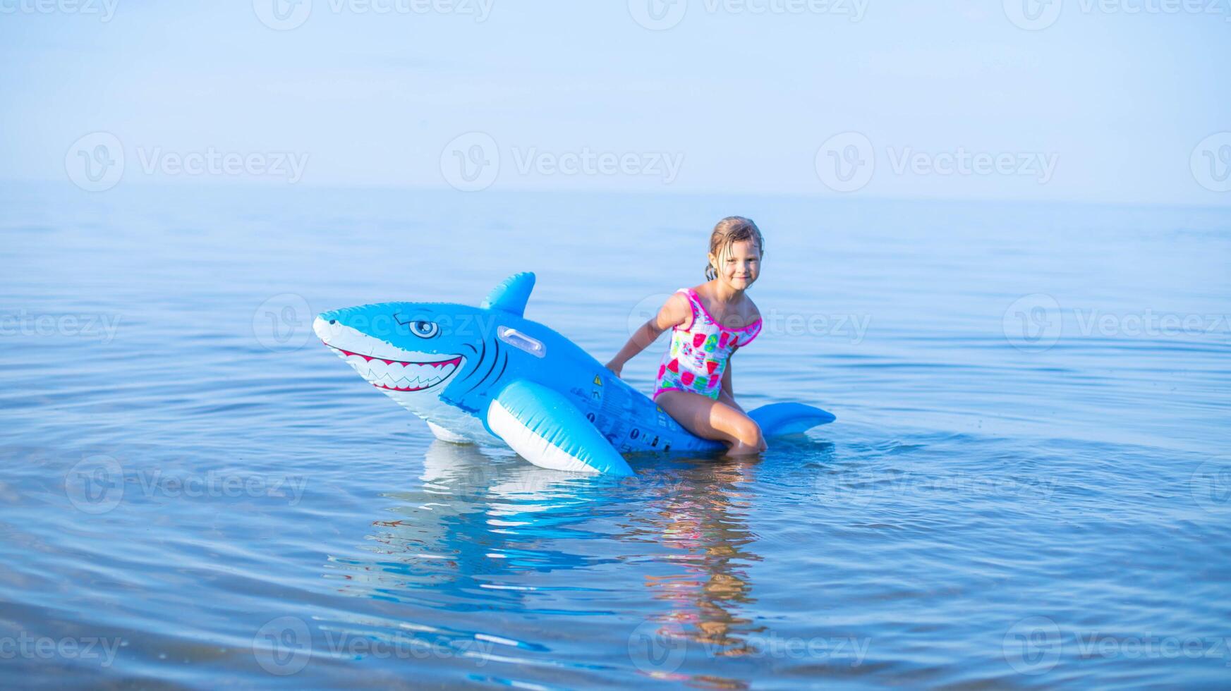 Happy girl of European appearance age of 7 swimming on an inflatable big shark toy in the sea.Family summer vocation concept. Copy space. photo