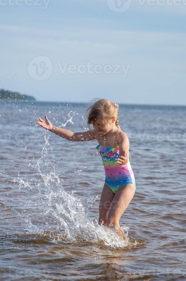 Young happy child girl of European appearance age of 6 having fun in water on the beach and splashing,tropical summer vocations,holidays.A child enjoys the sea.Vertical photo. photo