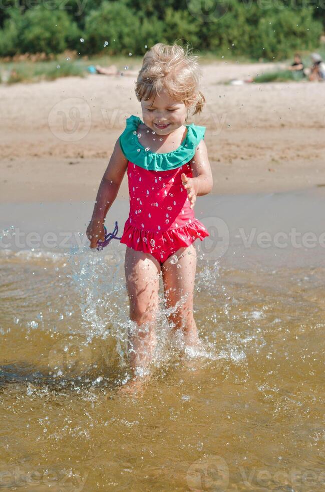 joven contento niño niña de europeo apariencia años de 4 4 teniendo divertido en agua en el playa y salpicaduras, tropicales verano vocaciones,vacaciones.a niño disfruta el mar.vertical foto. foto