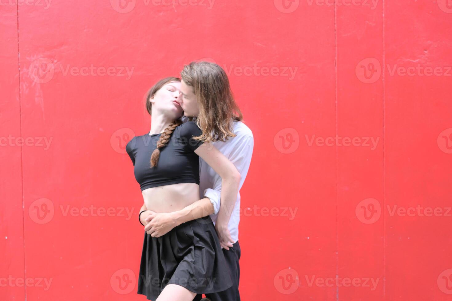 A couple is enjoying a summer vacation in the red wall background, happily showing their love to each other. photo
