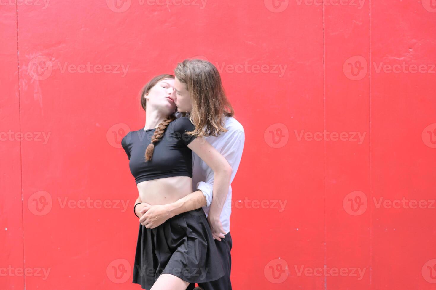 A couple is enjoying a summer vacation in the red wall background, happily showing their love to each other. photo