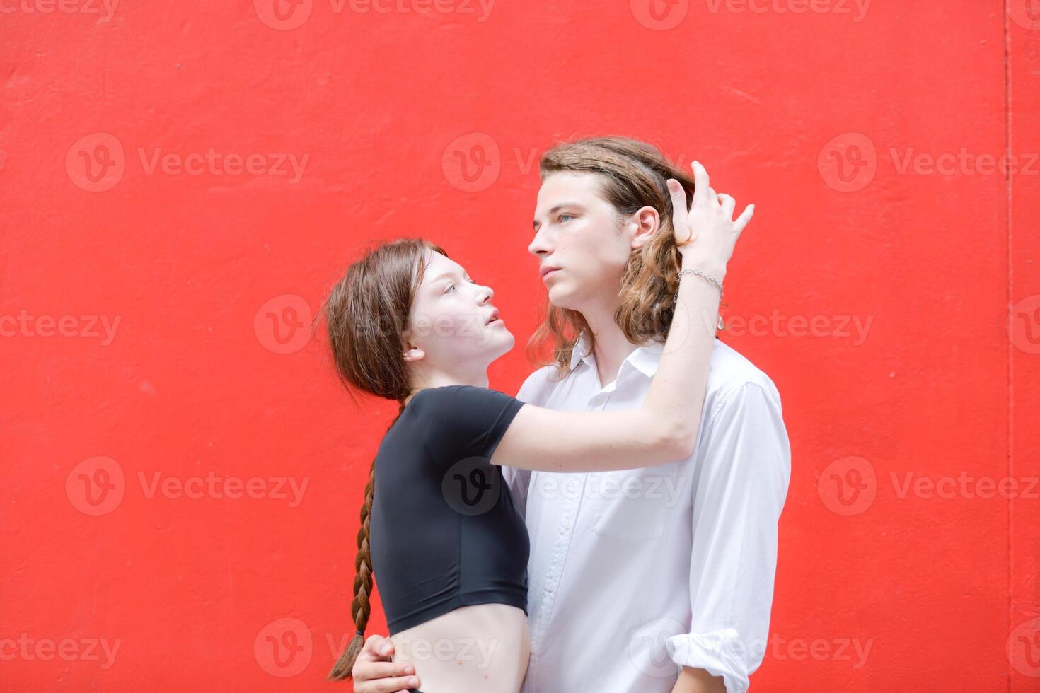 A couple is enjoying a summer vacation in the red wall background, happily showing their love to each other. photo